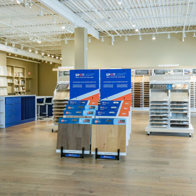 A retail showroom displaying various flooring samples, including wood-look planks and tiles, with 